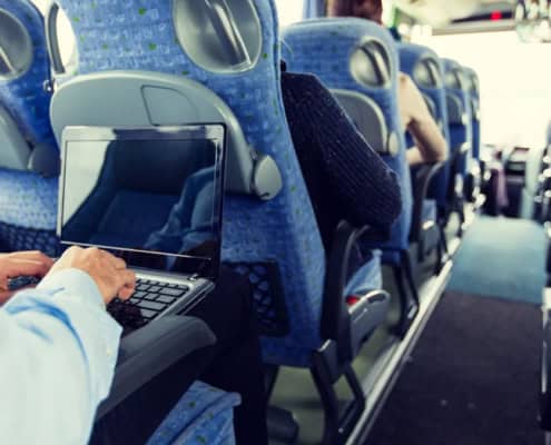 A person uses a laptop computer in their seat on a coach bus.