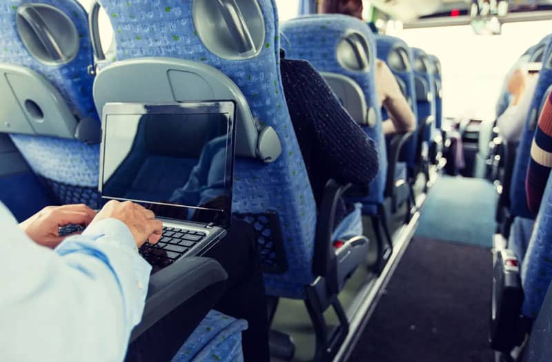 A person uses a laptop computer in their seat on a coach bus.