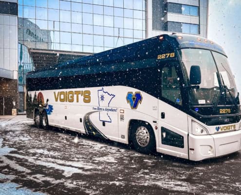 A charter bus is parked in front of a glass building while it snows.