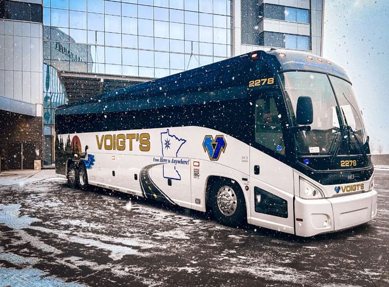 winter-travel A charter bus is parked in front of a glass building while it snows.