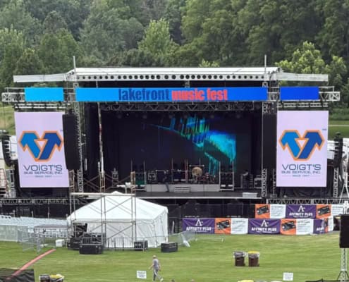 A musical festival stage featuring sponsor advertisements for Voigt’s Bus Service.