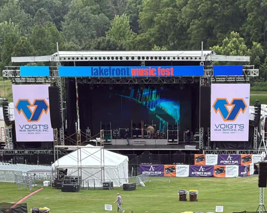 A musical festival stage featuring sponsor advertisements for Voigt’s Bus Service.