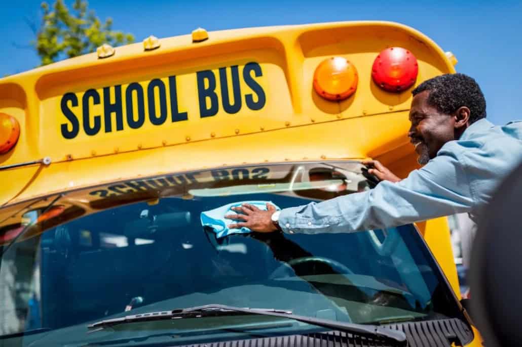 A bus driver washing a school bus windshield.