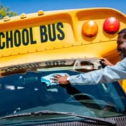 A bus driver washing a school bus windshield.