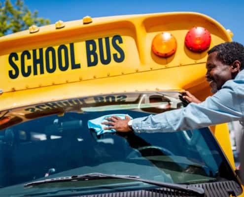 A bus driver washing a school bus windshield.