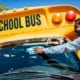 A bus driver washing a school bus windshield.