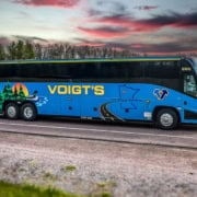 A Voigt’s charter bus on the road in front of a beautiful countryside sunset.