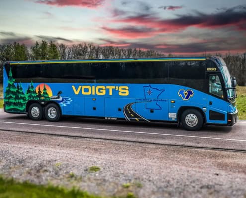 A Voigt’s charter bus on the road in front of a beautiful countryside sunset.