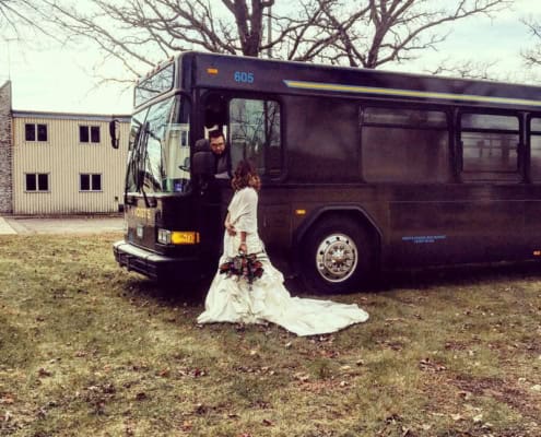 A woman in a wedding dress standing outside a charter bus.