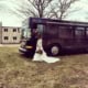 A woman in a wedding dress standing outside a charter bus.